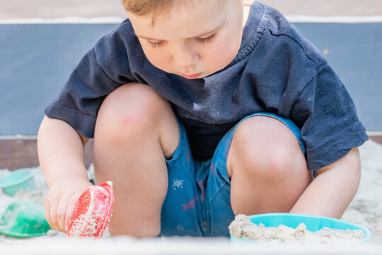 Little boy making an effort to lift a heavy bucket of sand.