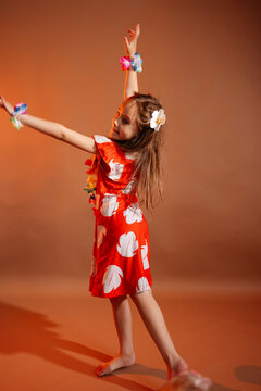 Pretty 6 years old girl in red dress with flowers is dancing in the photo studio with brown background. This photo has been taken in Prague, Czech Republic, August 2025