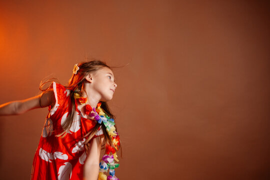 Pretty 6 years old girl in red dress with flowers is dancing in the photo studio with brown background. This photo has been taken in Prague, Czech Republic, August 2025
