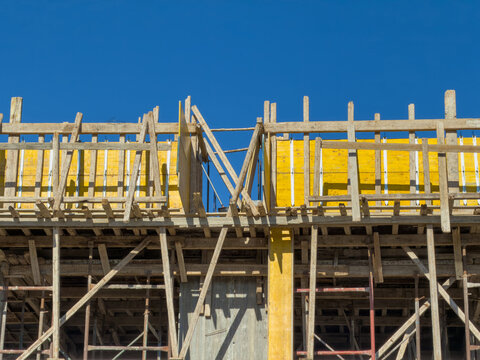 Timber supports and yellow formwork frame unfinished concrete structure, blue sky
