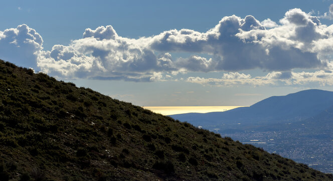 Towering cumulus clouds over golden sea and layered mountains,  view from Penteli mountain, Attica, Greece