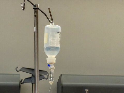 Intravenous fluid bottle and drip chamber hanging in quiet clinical treatment room