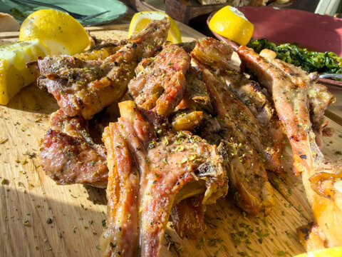 Browned herb-seasoned lamb chops with lemon wedges and saut ed greens on wooden board
