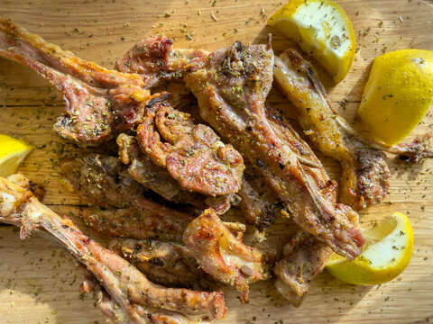 Rustic grilled lamb chops with oregano and lemon wedges on a wooden serving board