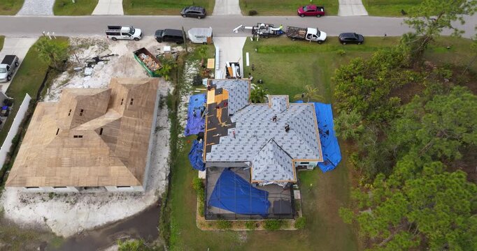 Asphalt shingles being applied to new home rooftop. Roofing workers securing shingles. Florida residential construction site.