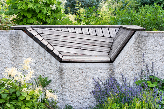 A geometric wood bench folds through an urban garden of gravel, where plants and greenery define landscape design through layered material and geometry.
