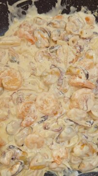 Creamy Seafood Simmers with Shrimp Mussels and Squid in a Dark Skillet, Overhead Closeup Shows Rich Sauce and Food Preparation Vertical video. Vertical video.
