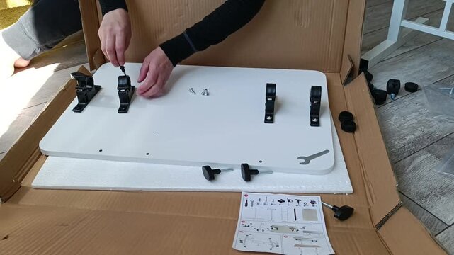 Person assembling flat pack furniture with tools and hardware on wooden floor