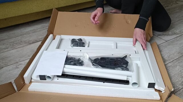 Person assembling flat pack furniture with tools and hardware on wooden floor
