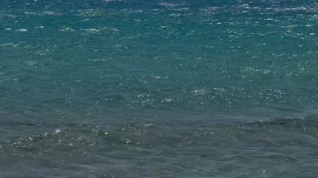 Crystal clear turquoise sea water with gentle ocean waves moving on the surface under sunlight. Natural marine background featuring sparkling reflections and calm wave motion, ideal f