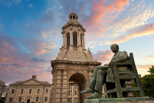 portrait shot of bronze statue of man seated in Trinity college Dublin campus with stone archway behind with golden dusk sunrise light