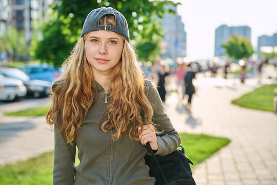 Happy teen girl with backpack and backward cap walking outdoors