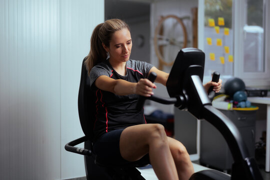 Struggling Woman Exercising On Recumbent Bike At Physical Therapy Clinic. Female patient performing rehabilitation training on stationary bicycle in modern recovery center 