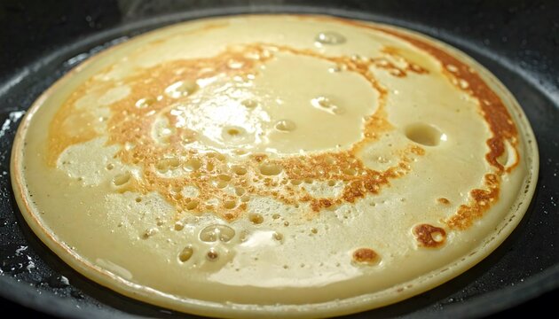 Close-up of a pancake sizzling and bubbling in a hot frying pan, showing the golden brown edges and surface texture.