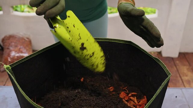 Gloved Hands Add Potting Soil to a Fabric Grow Bag on Wooden Deck, Overhead View Supporting Home Gardening and Plant Care