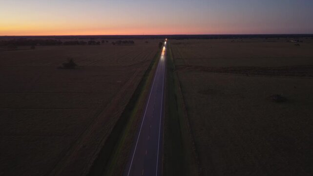 Quiet countryside highway with sparse traffic, glowing lights and dark surroundings, expressing calm, distance and late evening travel mood.