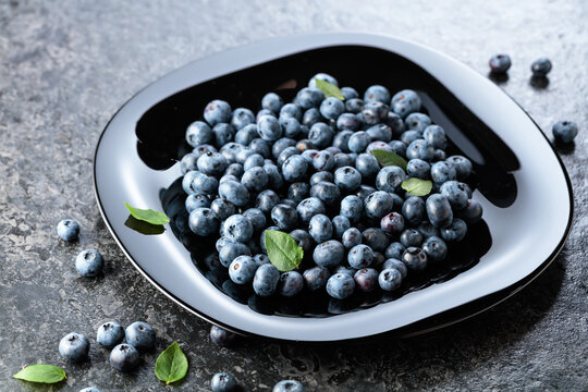 Blueberries with their leaves on a black plate.