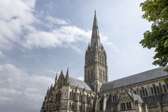 View of Salisbury Cathedral with its iconic spire rising against a blue sky with light clouds in Salisbury, England, United Kingdom.