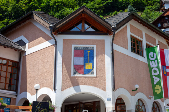 Hallstatt Town Hall with Coat of Arms Mosaic and ADEG Supermarket Flags. Hallstatt, Austria - June 22, 2026