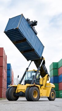 Yellow forklift crane lifts blue shipping container high in industrial port yard surrounded by stacked cargo boxes
