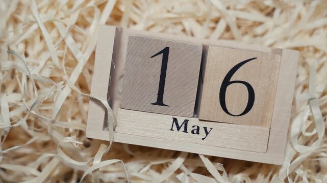 Wooden calendar blocks showing date May 16 on natural wood shavings background