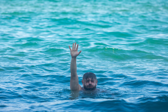 Male swimmer raises hand above turquoise ocean water, signaling for attention. Clear, sunny day with gentle waves, ideal for rescue, safety, and beach themes.