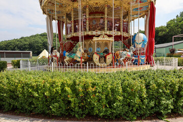 Two story vintage carousel featuring decorated horses and carriages stands surrounded by neat green bushes in an amusement park. © Олег Струс