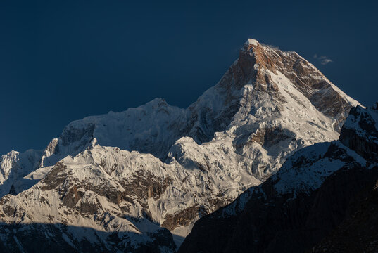 View of the snow-capped peak of Mashabrum mountain in the Karakoram Range, illuminated by sunlight against a dark sky, Karakoram Range, Gilgit Baltistan, Pakistan.