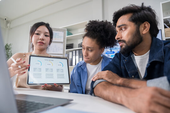 Three professional colleagues looking at a laptop screen together, discussing project details during an online video conference with a client.