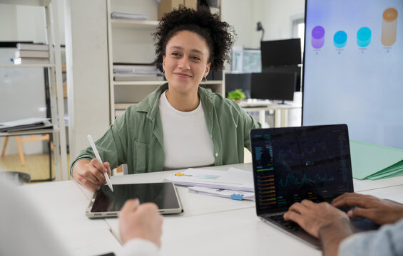 Smiling businesswoman discussing financial data and graphs during team meeting.