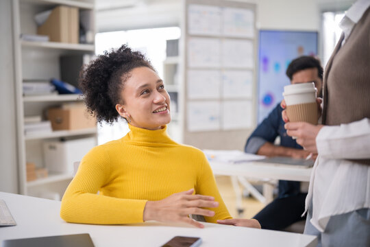 Cheerful businesswoman discussing project with colleague during office coffee break.