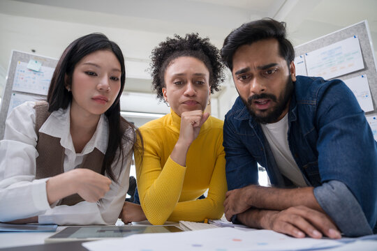 Three professional colleagues leaning forward and looking seriously at documents on the desk during a brainstorming session.