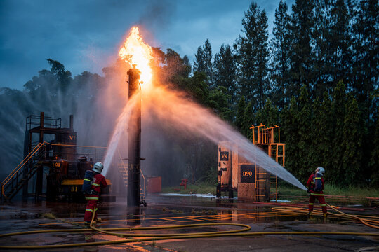 Firefighter Team Fighting a Large Industrial Fire with Powerful Water Streams and Hoses across a Wet Emergency Response Site