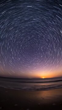 Long exposure star trails rotating over a calm ocean beach at night.