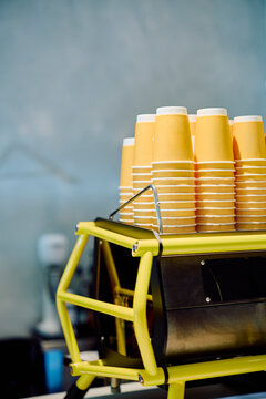 Stacks of yellow paper cups awaiting hot beverages on a modern espresso machine in a cafe setting, ready for service