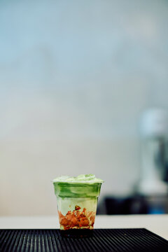 Layered iced matcha latte with creamy green tea foam and crunchy brown crumbs, offering a refreshing sweet beverage