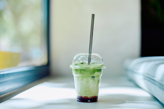 Refreshing layered iced matcha latte with berry syrup in a plastic cup, featuring a reusable metal straw, sitting by a window