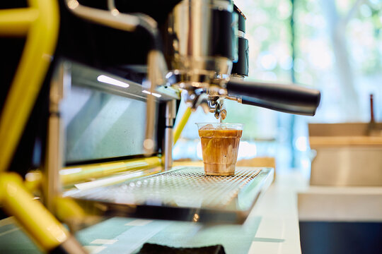 Espresso machine brewing a refreshing iced coffee latte into a plastic cup, perfect for a summer drink