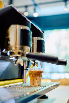 Espresso machine dispensing fresh coffee into a cup with ice and milk, creating a refreshing iced latte in a cafe setting