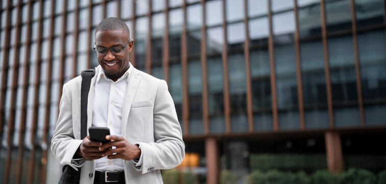 Entrepreneur, black businessman, using smartphone, texting, outdoor near office building. African american business man smiling, staying connected with technology, innovating. Copy space. Web banner.