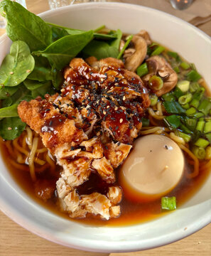 A steaming bowl of ramen with chicken and vegetables on a wooden table
