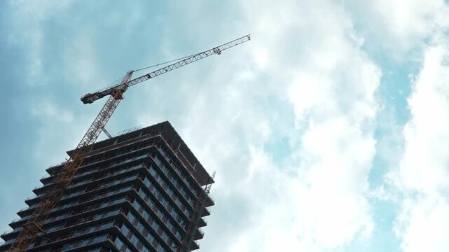 Construction crane building modern skyscraper against cloudy sky.