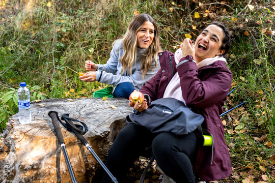 Friends laughing and relaxing during autumn nordic walking break, enjoying healthy snack