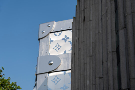 Architectural detail of a luxury fashion store facade designed as a giant metallic trunk with monogram pattern under a clear blue sky in Paris