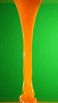 Abstract macro shot of vibrant orange liquid pouring against a solid green background.