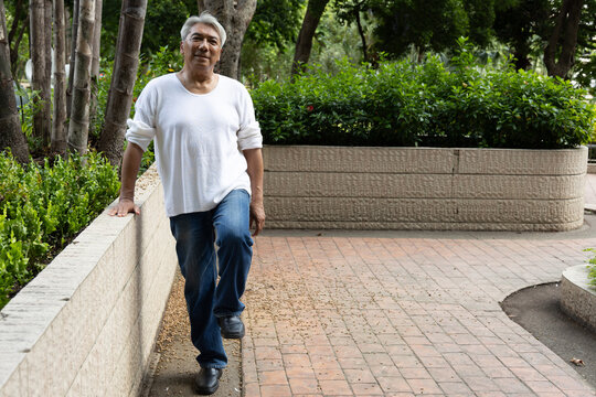 asian senior man lifting one foot off the ground for balance training in an urban park, functional fitness for healthy aging