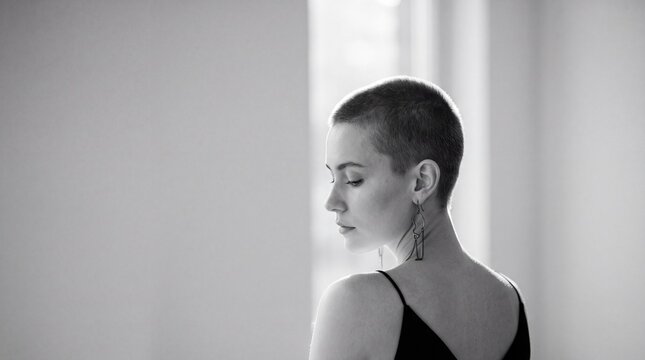 Resilience Embodied: A young woman with a shaved head, her eyes closed in quiet contemplation, stands in soft, natural light. The image captures a powerful sense of inner strength and self-acceptance.