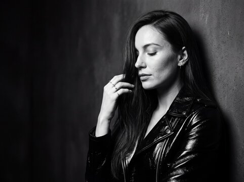 Melancholy Muse: A pensive young woman with her eyes closed, her hand gently touching her hair, leans against a textured wall. Her expression evokes a sense of introspection and quiet contemplation.