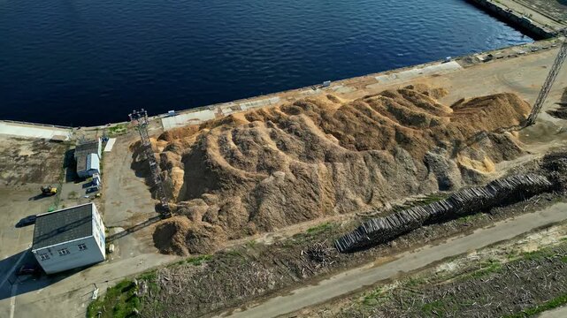 Aerial view of large piles of wood chips and stacked logs at a port facility in Latvia.