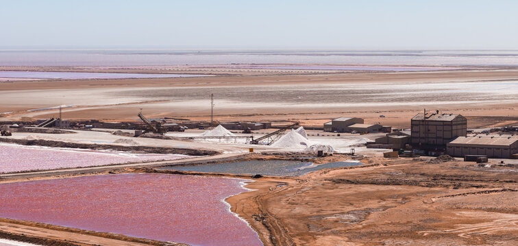 Aerial view of industrial salt production facilities, pink evaporation ponds, and white salt piles in the desert landscape of Walvis Bay, Namibia.